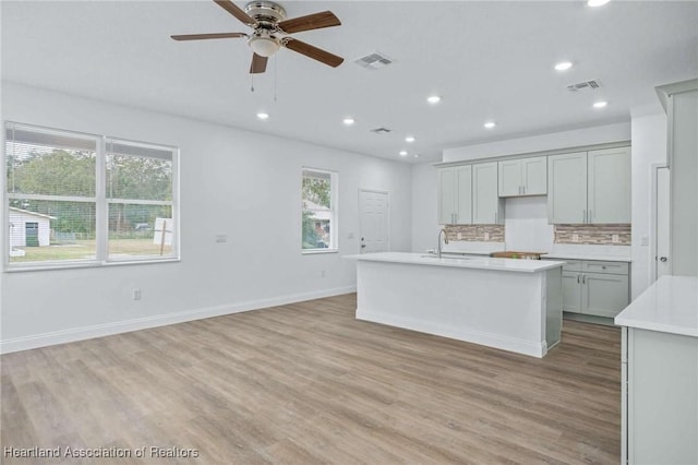 kitchen with a wealth of natural light, gray cabinetry, light hardwood / wood-style flooring, and a center island with sink