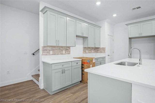 kitchen featuring gray cabinets, hardwood / wood-style floors, tasteful backsplash, and sink