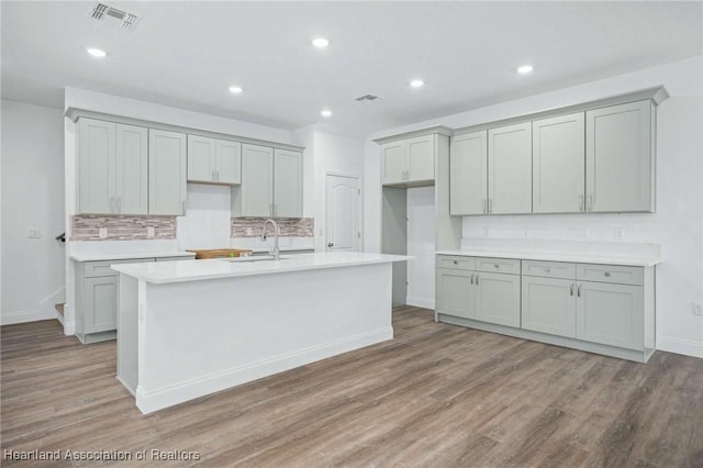 kitchen featuring sink, decorative backsplash, hardwood / wood-style floors, and a kitchen island with sink