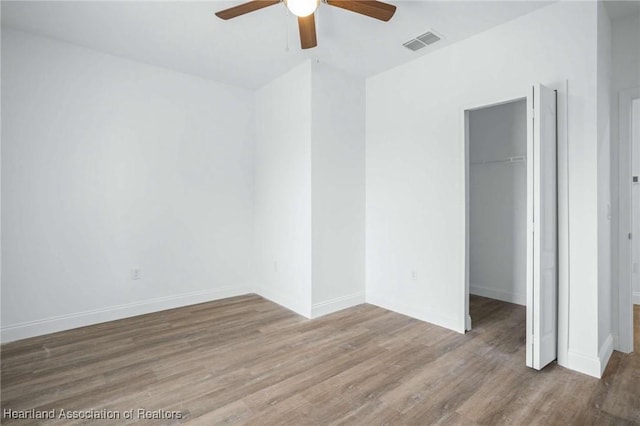 unfurnished bedroom featuring ceiling fan, hardwood / wood-style floors, a closet, and a walk in closet