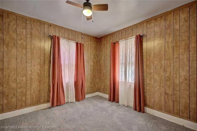 carpeted spare room featuring ceiling fan and wood walls