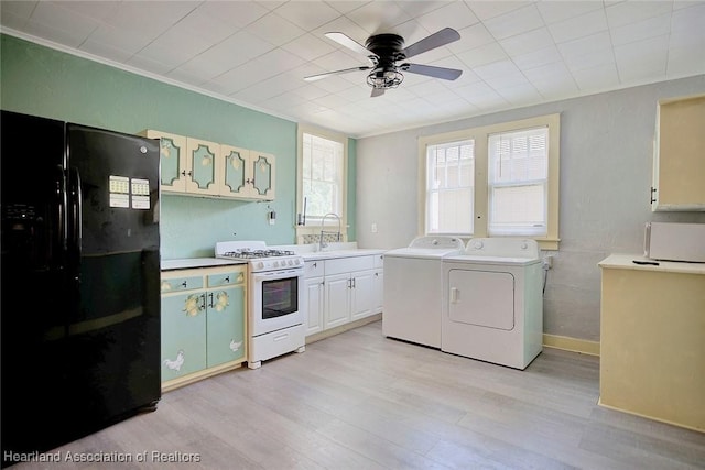 kitchen featuring ceiling fan, washing machine and dryer, light hardwood / wood-style flooring, black refrigerator, and white gas range oven