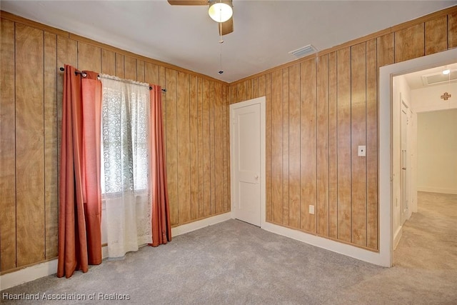 carpeted empty room featuring ceiling fan and wood walls