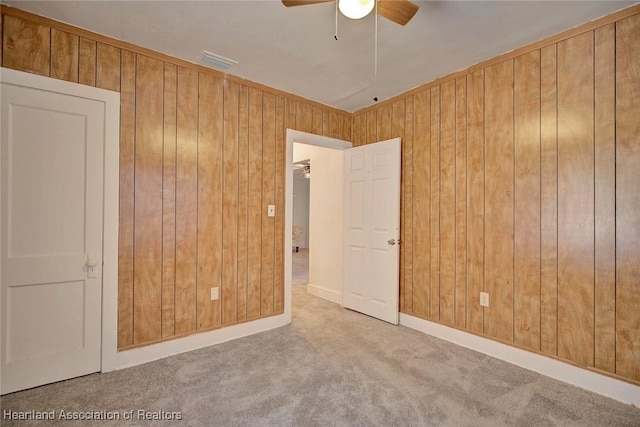 carpeted spare room with ceiling fan and wood walls