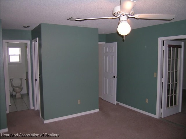 unfurnished bedroom with a textured ceiling, a ceiling fan, visible vents, baseboards, and carpet