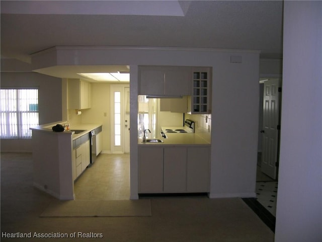 kitchen featuring a peninsula, a sink, light countertops, stainless steel dishwasher, and glass insert cabinets