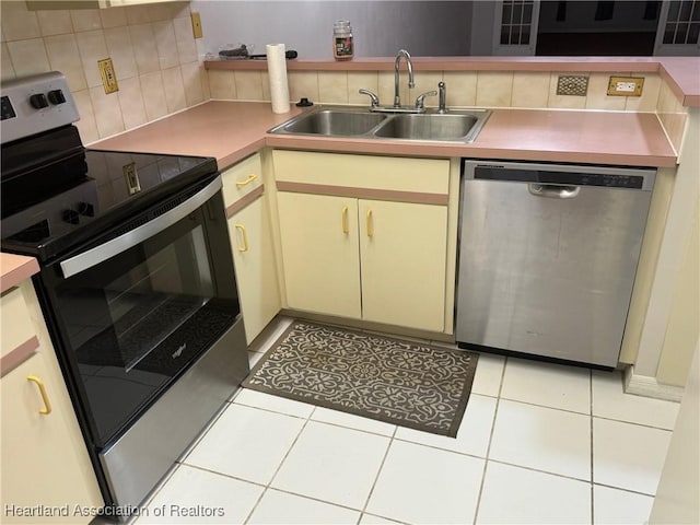 kitchen with appliances with stainless steel finishes, cream cabinetry, light tile patterned flooring, and a sink