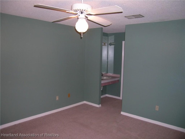 unfurnished bedroom with a textured ceiling, carpet floors, a ceiling fan, visible vents, and baseboards