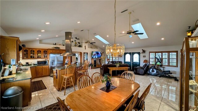 tiled dining space featuring ceiling fan with notable chandelier, a skylight, and high vaulted ceiling