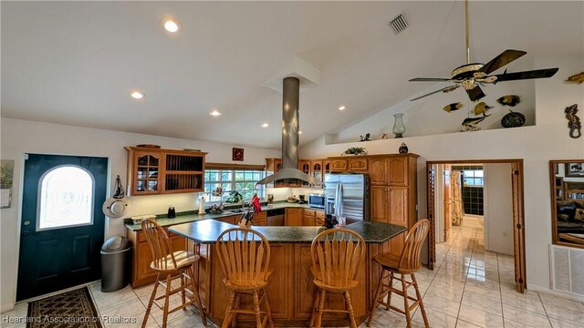 kitchen featuring a breakfast bar, stainless steel appliances, vaulted ceiling, ceiling fan, and island range hood