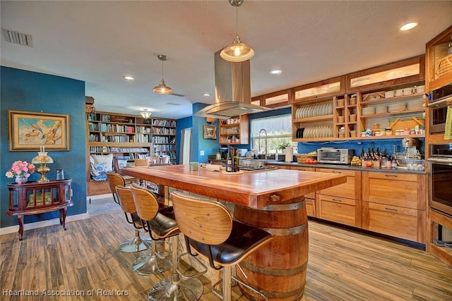 kitchen featuring stainless steel oven, island range hood, hanging light fixtures, light hardwood / wood-style floors, and butcher block counters