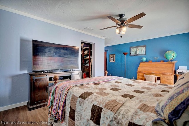 bedroom featuring a walk in closet, a textured ceiling, ceiling fan, crown molding, and wood-type flooring