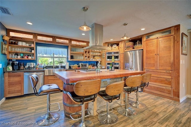 kitchen featuring built in shelves, hanging light fixtures, stainless steel appliances, light hardwood / wood-style flooring, and island range hood