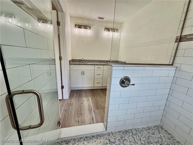 bathroom featuring visible vents, vanity, wood finished floors, tiled shower, and a textured ceiling