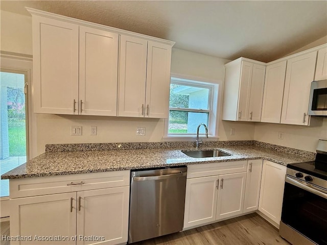 kitchen with light stone countertops, appliances with stainless steel finishes, a sink, light wood-style flooring, and white cabinetry