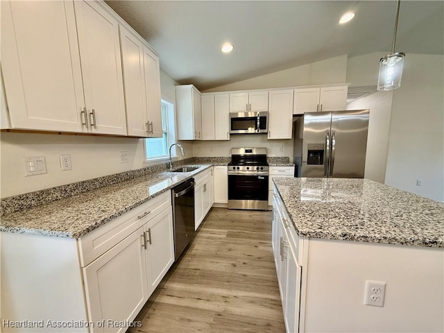kitchen featuring appliances with stainless steel finishes, light wood-type flooring, a sink, lofted ceiling, and white cabinetry