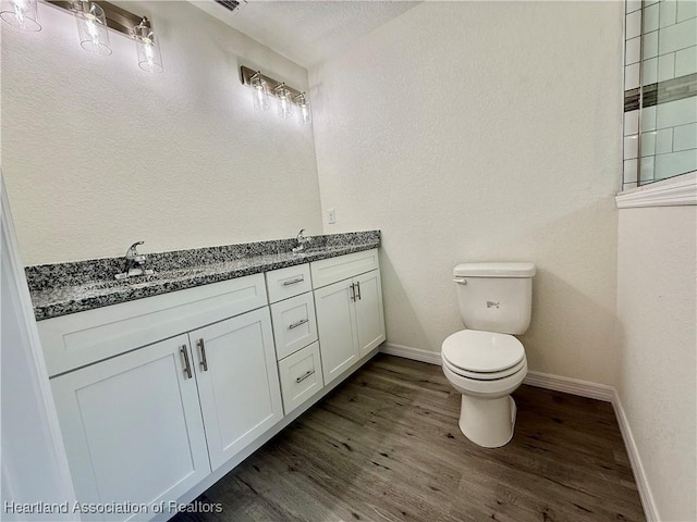 bathroom featuring double vanity, wood finished floors, a sink, baseboards, and toilet