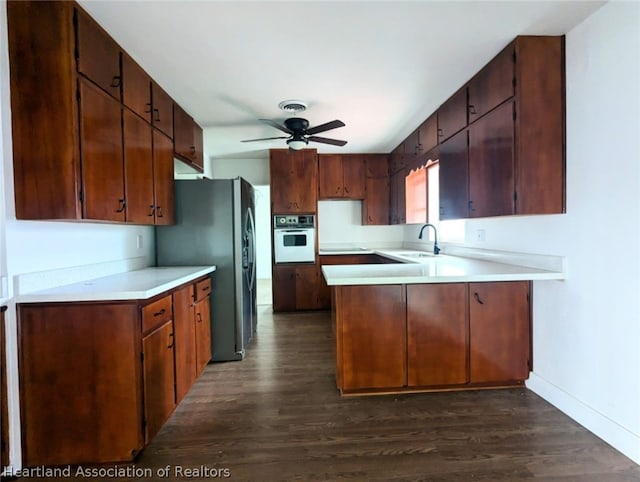 kitchen with kitchen peninsula, stainless steel fridge, ceiling fan, dark wood-type flooring, and oven