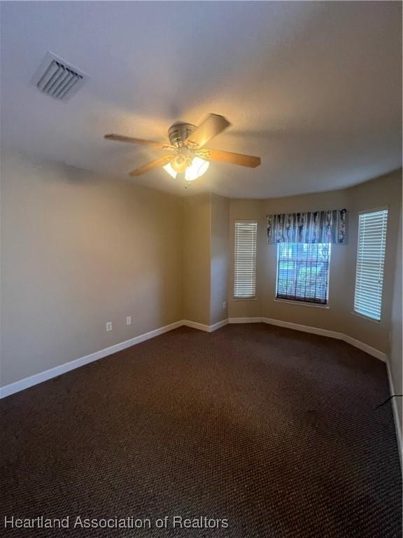 spare room with ceiling fan and dark carpet