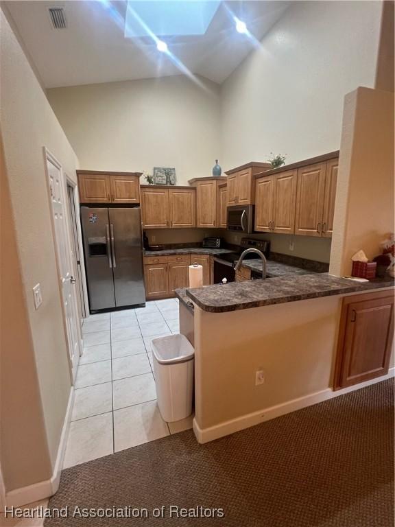 kitchen featuring kitchen peninsula, light tile patterned floors, a high ceiling, and appliances with stainless steel finishes