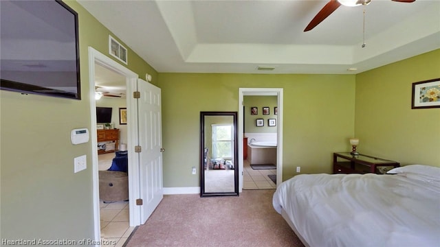 bedroom featuring light tile patterned floors, a tray ceiling, ensuite bath, and ceiling fan