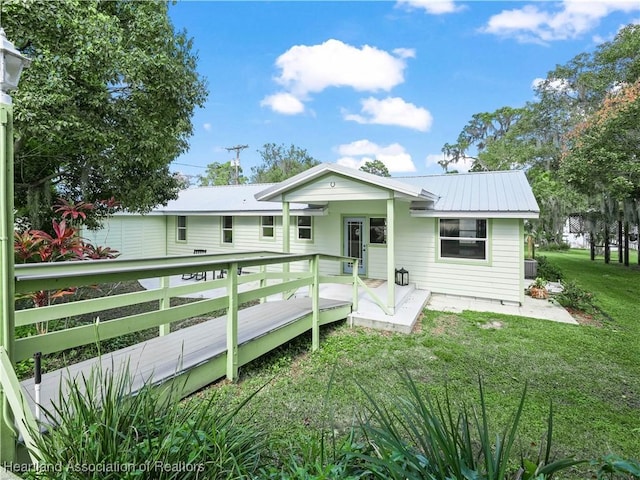 view of front facade with central air condition unit, metal roof, a deck, and a front lawn