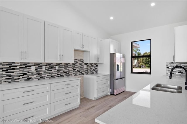 kitchen featuring sink, white cabinetry, stainless steel fridge, light hardwood / wood-style floors, and decorative backsplash