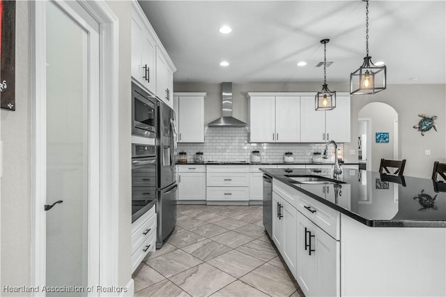 kitchen featuring pendant lighting, sink, appliances with stainless steel finishes, white cabinetry, and wall chimney exhaust hood