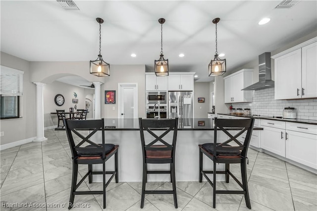 kitchen with wall chimney exhaust hood, stainless steel appliances, hanging light fixtures, and a center island with sink