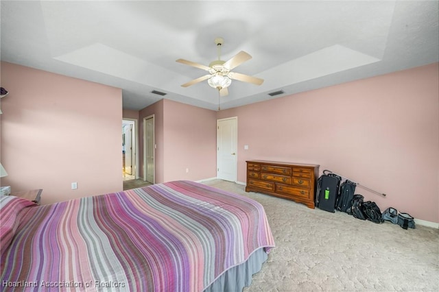 bedroom featuring light carpet, connected bathroom, a raised ceiling, and ceiling fan