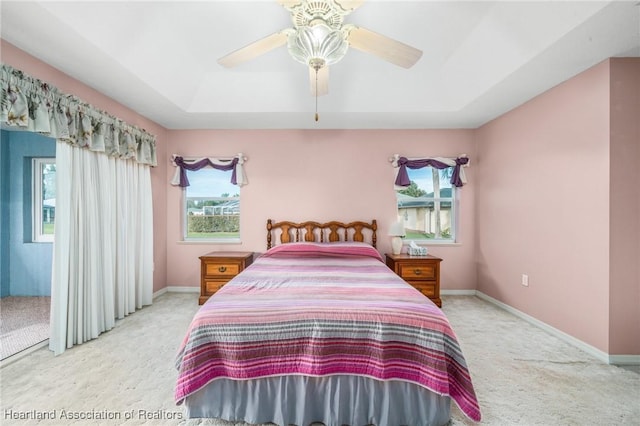 bedroom with light carpet, a raised ceiling, and ceiling fan