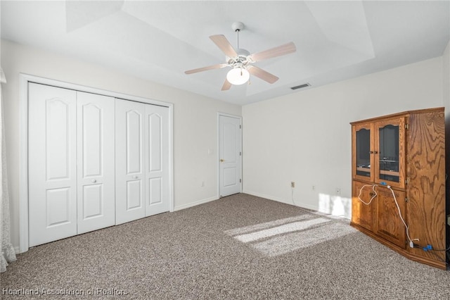 unfurnished bedroom with carpet floors, a closet, a raised ceiling, and ceiling fan