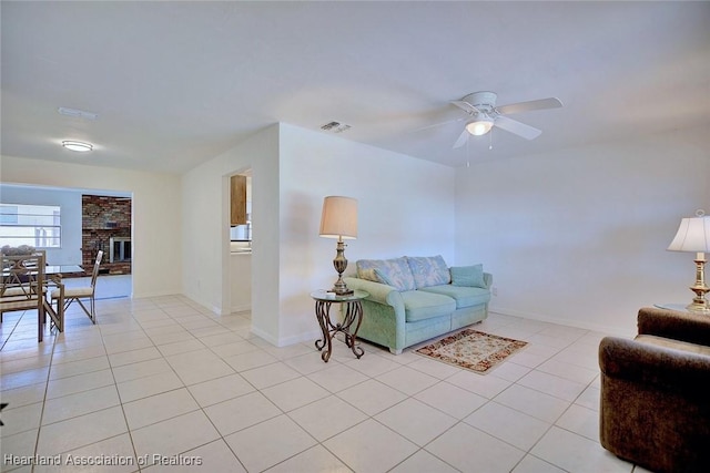 living room featuring light tile patterned floors, ceiling fan, a fireplace, visible vents, and baseboards