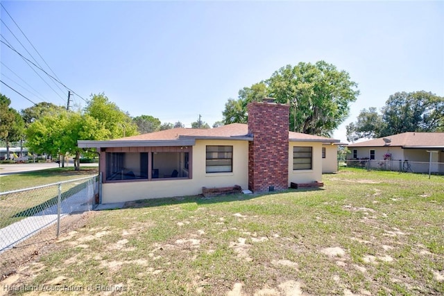 rear view of house with a sunroom, a chimney, fence, a yard, and stucco siding