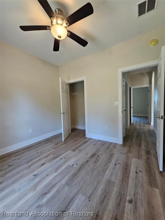 unfurnished bedroom featuring visible vents, baseboards, a closet, ceiling fan, and wood finished floors