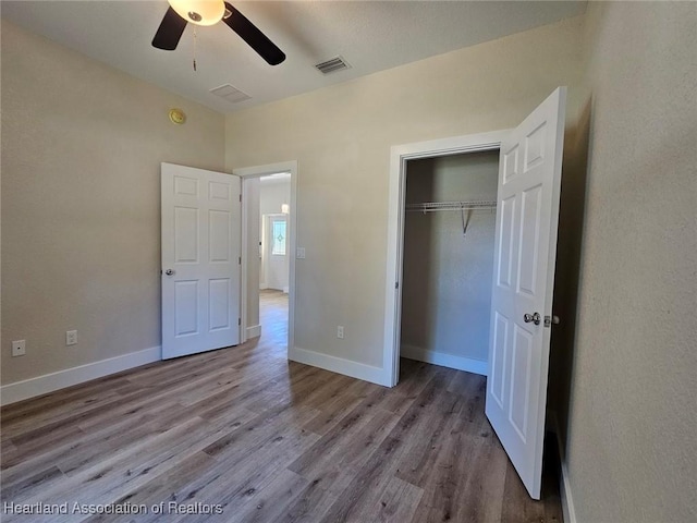 unfurnished bedroom featuring a closet, a ceiling fan, visible vents, wood finished floors, and baseboards
