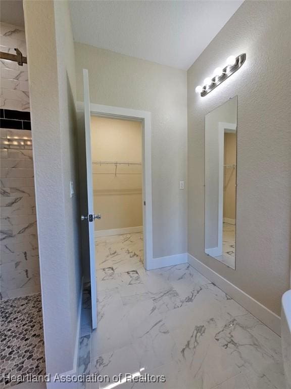 full bath featuring a tile shower, marble finish floor, baseboards, and a walk in closet