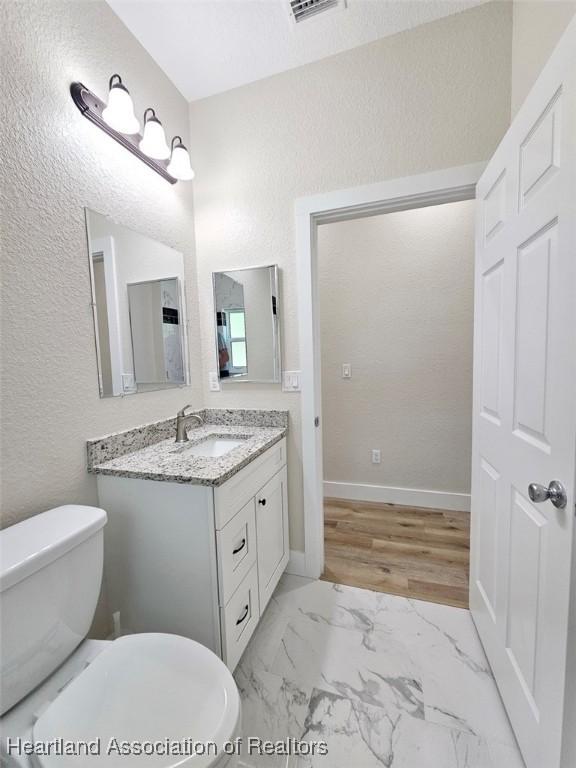 bathroom featuring vanity, baseboards, a textured wall, toilet, and marble finish floor
