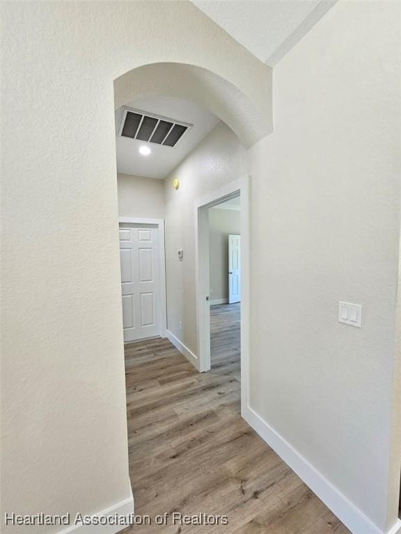 hall with visible vents, baseboards, arched walkways, and wood finished floors