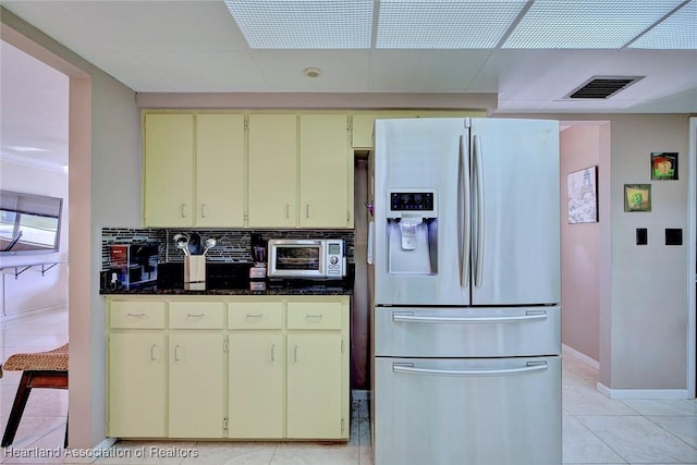 kitchen featuring stainless steel refrigerator with ice dispenser, visible vents, backsplash, light tile patterned flooring, and baseboards