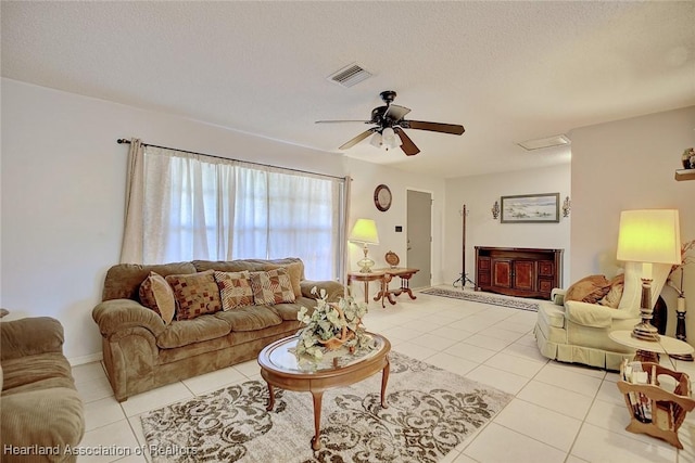 living room with a textured ceiling, ceiling fan, light tile patterned flooring, visible vents, and attic access