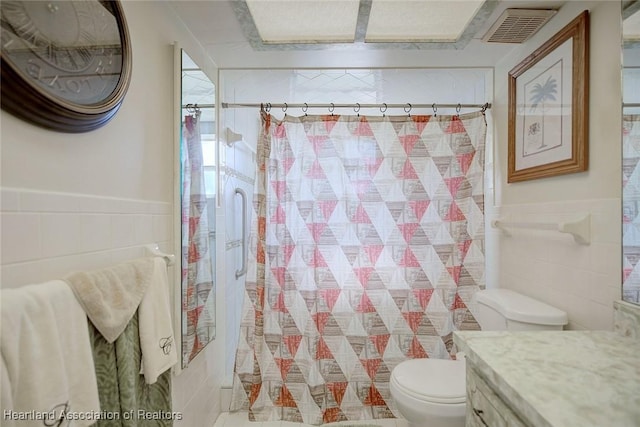 bathroom with visible vents, toilet, a shower with curtain, vanity, and tile walls