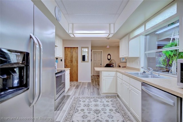 kitchen with appliances with stainless steel finishes, light countertops, light wood-style floors, white cabinetry, and a sink