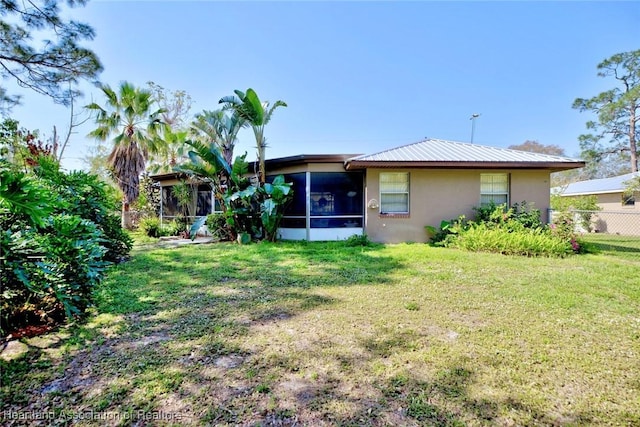 back of property with a yard, stucco siding, a sunroom, fence, and metal roof