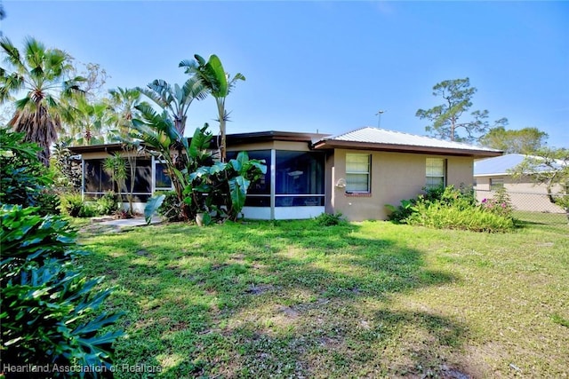 rear view of house featuring a sunroom, fence, stucco siding, and a yard