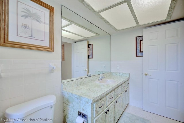 bathroom with toilet, wainscoting, vanity, and tile walls