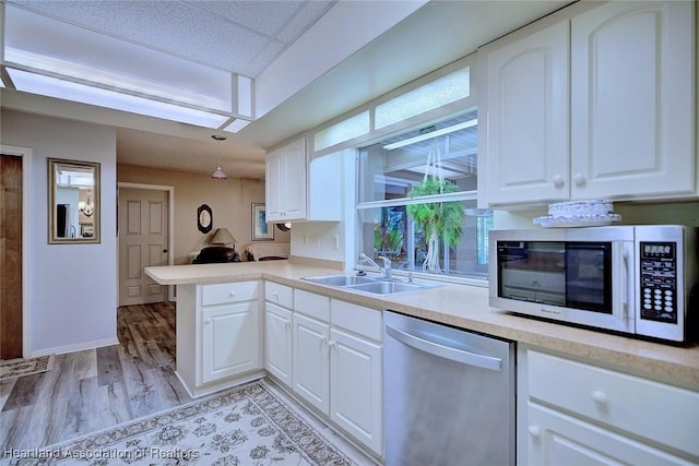 kitchen featuring dishwasher, a peninsula, light countertops, white cabinetry, and a sink