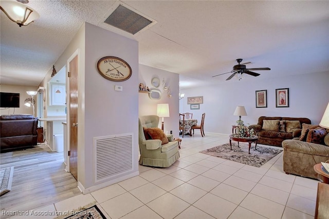 living area with a ceiling fan, visible vents, a textured ceiling, and light tile patterned floors