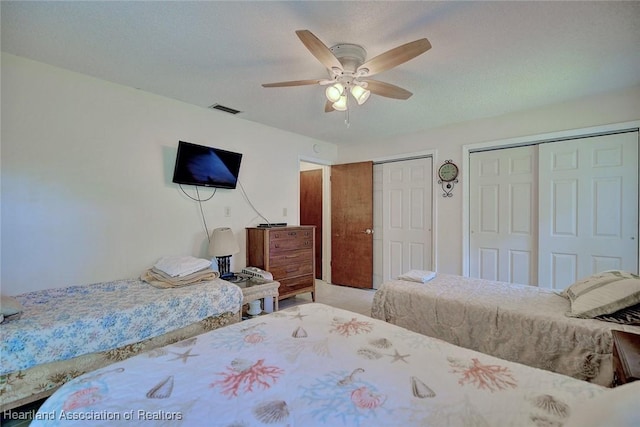 bedroom featuring visible vents, ceiling fan, and two closets