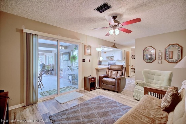 living area featuring light wood-type flooring, a ceiling fan, visible vents, and a textured ceiling